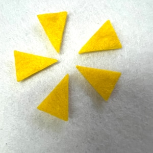 May include: Six yellow felt triangles arranged in a star shape on a white background.