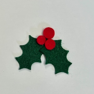 May include: A felt holly sprig with three red berries. The holly leaves are dark green with pointed edges. The berries are round and a vibrant red. This festive decoration is perfect for holiday crafts and decor.