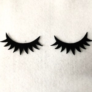 May include: Two black felt eyelashes, each with a curved shape and a row of pointed lashes.