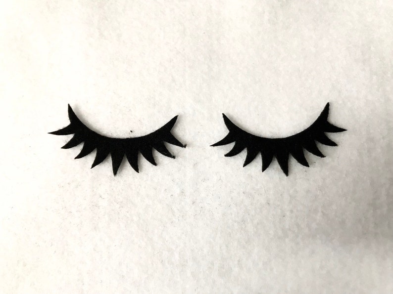 May include: Two black felt eyelashes, each with a curved shape and a row of pointed lashes.