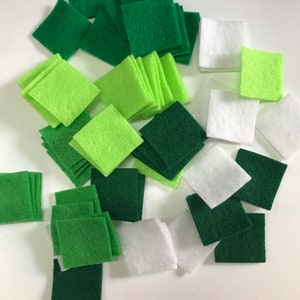 May include: A collection of felt squares in various shades of green, white, and lime green. The squares are arranged in a random pattern on a white surface.