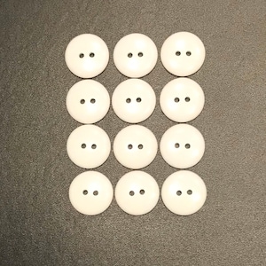 May include: Twelve white plastic buttons with two holes each. The buttons are arranged in three rows of four.