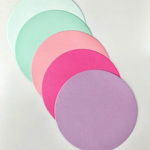 May include: Five round paper circles in different pastel colors, stacked on top of each other. The colors are white, light green, pink, hot pink, and lavender.