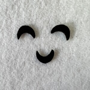 May include: A simple black felt smiley face with two crescent-shaped eyes and a curved mouth.