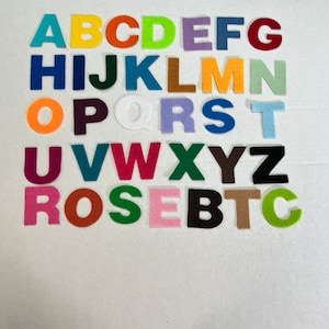 May include: Felt alphabet letters in various colors, including red, orange, yellow, green, blue, purple, brown, and black. The letters are arranged in alphabetical order, with the letters "ROSE" and "BTC" in a separate row below.