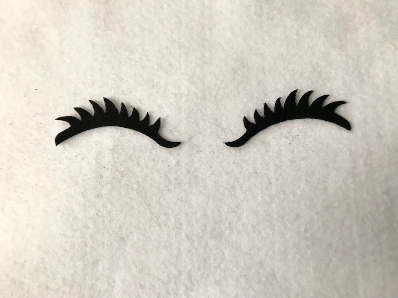 May include: Two black felt eyelashes with a jagged edge, on a white background.