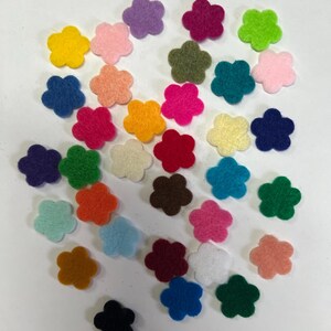 May include: A collection of small, five-petaled flower shapes made of felt in a wide variety of vibrant colors including red, blue, yellow, green, orange, purple, pink, brown, black, white, and various pastel shades scattered across the frame.