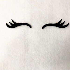 May include: Two black eyelashes, each with three points, are arranged in a curved shape, resembling a pair of eyes. The eyelashes are on a white background.