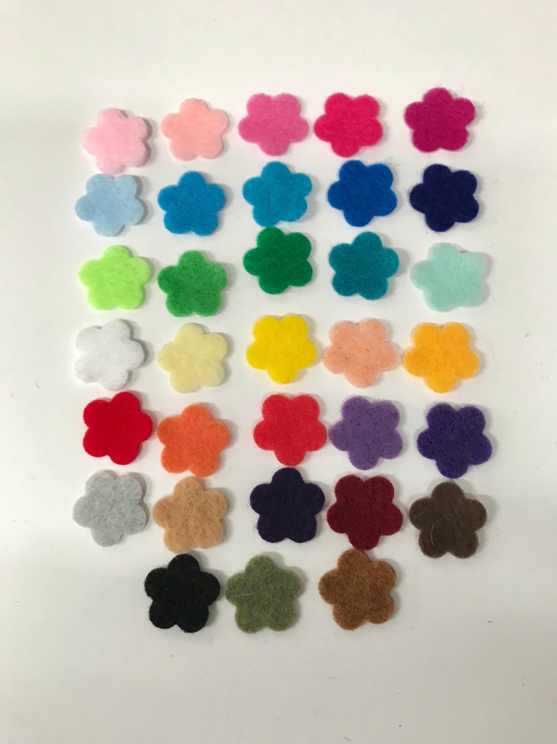 May include: A collection of thirty-three small, five-petaled flower shapes cut from felt fabric. The flowers are arranged in a grid and feature a wide variety of solid colors, including shades of pink, blue, green, yellow, orange, red, purple, brown, gray, black, and white.