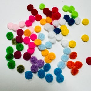 May include: A collection of small, round, colorful felt pom-poms scattered on a white surface. The pom-poms are in various shades of red, pink, orange, yellow, green, blue, and purple. These craft supplies are ideal for DIY projects.
