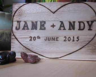 Puede incluir: Una caja de madera blanca con un corazón quemado en la parte delantera. El corazón contiene el texto "JANE + ANDY" y "20th JUNE 2015".