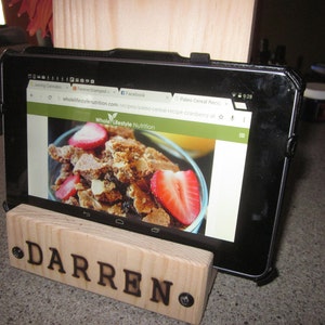May include: A wooden tablet stand with the name "Darren" engraved on it. A black tablet is in the stand, displaying a website for "Whole Lifestyle Nutrition" with a recipe for Paleo Cereal with Cranberries.