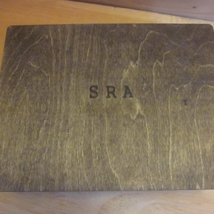 May include: A dark brown wooden box with the letters "SRA" engraved on the front.