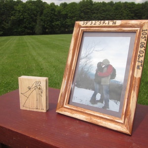 May include: A wooden picture frame with a photo of a couple kissing in the snow. The frame has the coordinates "39°32'59.1"N 105°06'02.7"W" engraved on it.