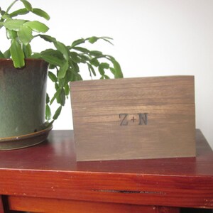 Puede incluir: Una caja de madera con las iniciales "Z+N" grabadas en la parte delantera. La caja es marrón y tiene una veta de madera natural.