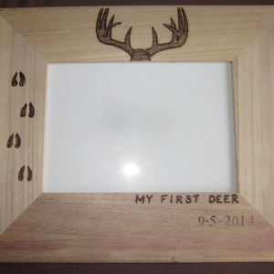 Puede incluir: Un marco de fotos de madera con un diseño de asta de ciervo y huellas de ciervo en el lateral. El marco tiene el texto "MY FIRST DEER" y "9-5-2014" inscrito en la parte inferior.