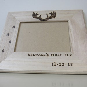 Könnte beinhalten: Ein Holzbildrahmen mit einem eingebrannten Design aus Geweih und einem Hirschfußabdruck. Der Rahmen trägt die Inschrift "KENDALL'S FIRST ELK" und "11-12-18".