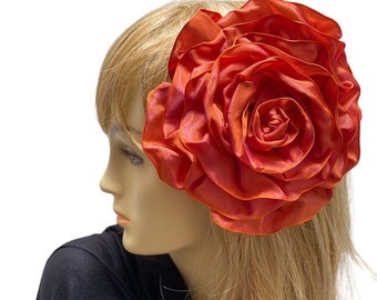 May include: A large, bright orange silk flower hair clip. The flower is made of multiple layers of fabric and has a slightly ruffled texture.