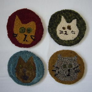 May include: Four round, hand-stitched cat-themed rug ornaments. The rugs are in shades of red, green, blue, and brown. Each rug features a different cat face with unique details.