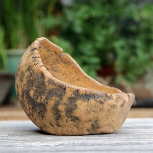 Op de afbeelding: Een handgemaakte, rustieke, bruine keramische kom met een organische vorm. De kom heeft een getextureerd oppervlak met donkerbruine markeringen en een ruwe rand. Ideaal voor kleine planten of decoratieve doeleinden.