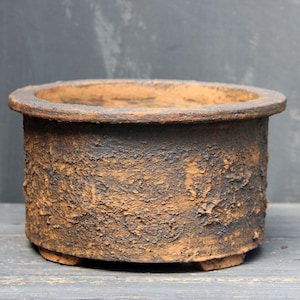 Pode incluir: Um vaso redondo de cerâmica castanha e preta texturizada com uma borda larga. O vaso tem uma aparência áspera e envelhecida e assenta em três pequenos pés. Ideal para suculentas ou plantas pequenas.