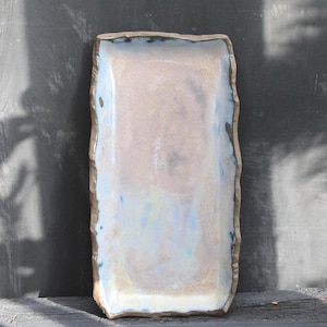 Puede incluir: Plato rectangular de cerámica para servir con un esmalte rosa claro y azul. Los bordes tienen una textura rugosa y orgánica con un borde marrón. El plato está diseñado para servir alimentos.