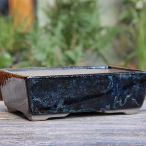 Könnte beinhalten: Ein rechteckiger Bonsai-Topf mit dunkelblauer Glasur und einem hellgrauen Rand. Der Topf hat eine strukturierte Oberfläche und ist aus Keramik.