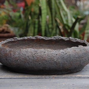 May include: A handcrafted, dark brown, textured ceramic bowl with a rough, uneven rim. The bowl has a wide, shallow design, perfect for displaying plants or as a decorative piece. The bowl is approximately 12 inches in diameter.