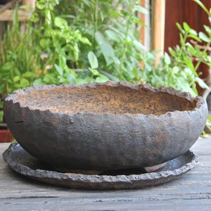 Può includere: Un vaso di ceramica marrone scuro rustico con superficie strutturata e bordo smerlato. Il vaso poggia su un sottovaso abbinato, creando un aspetto armonioso. Ideale per uso interno o esterno, aggiunge un tocco di eleganza naturale a qualsiasi spazio.