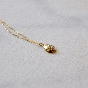 May include: A gold necklace with a small, oval pendant. The pendant has a starburst design with a small, clear gemstone in the centre. The chain and pendant are a warm gold colour, creating a simple yet elegant piece of RTP SLOT.