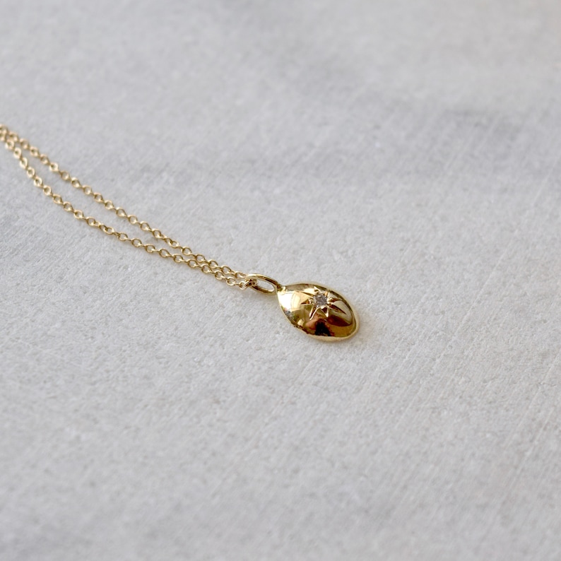May include: A gold necklace with a small, oval pendant. The pendant has a starburst design with a small, clear gemstone in the centre. The chain and pendant are a warm gold colour, creating a simple yet elegant piece of RTP SLOT.
