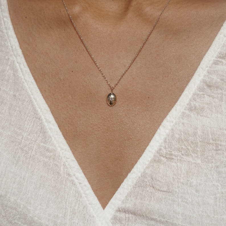 May include: A fine gold necklace with a small, oval pendant. The pendant has a subtle design, hanging from a delicate chain. The necklace is worn against a white top.