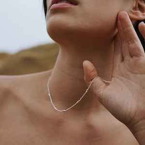 May include: A silver chain necklace with small beads. The necklace is delicate and simple.
