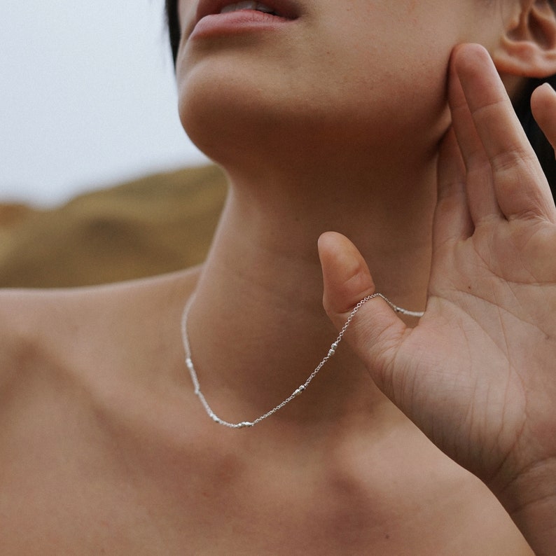 May include: A silver chain necklace with small beads. The necklace is delicate and simple.