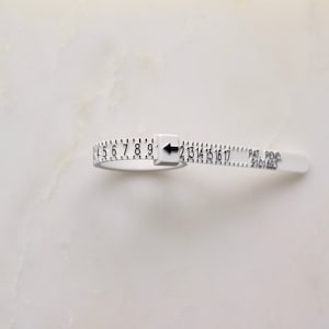 May include: White plastic ring sizer with black markings and a black arrow pointing to the number 10. The sizer has the text "PAT. PEND. 9101683" printed on it.