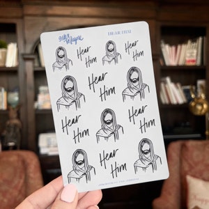 Peut inclure: Une feuille d'autocollants avec une illustration en noir et blanc d'un homme barbu et le texte "Hear Him" r&eacute;p&eacute;t&eacute; plusieurs fois.