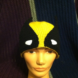 May include: A yellow and black crocheted hat with a white eye design. The hat is worn on a mannequin head.