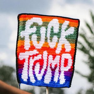 Peut inclure: Panneau carré fait à la main avec les mots "FUCK TRUMP" en blanc sur un fond arc-en-ciel. Le panneau a une bordure noire et est tenu par un bâton en bois.