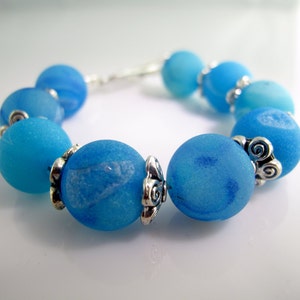 May include: A bracelet made of light blue glass beads with silver accents. The beads have a marbled effect.