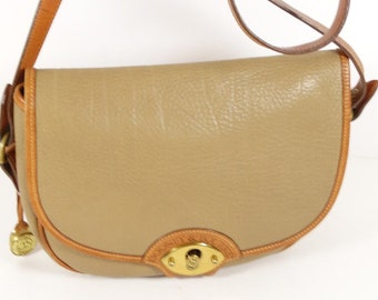 May include: A tan leather crossbody bag with a brown leather strap and gold hardware. The bag has a flap closure with a gold buckle and a small gold charm attached to the bottom.