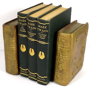 May include: Three green hardcover books with gold lettering titled "Mark Twain" and "The Prince and the Pauper". The books are used as bookends with a gold decorative bookend on the right.