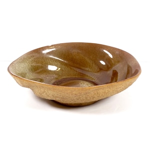May include: A brown ceramic bowl with a textured exterior and a smooth, glossy interior. The bowl has an irregular shape and a slightly wavy rim.