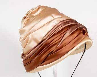 May include: A brown and beige satin hat with a wide brim, displayed on a metal stand.
