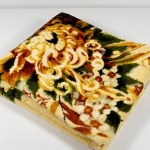 May include: A folded yellow, green, and brown patterned throw blanket with a floral design.