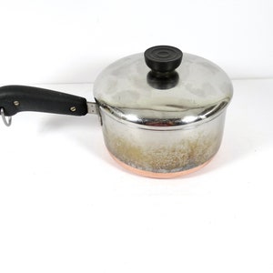 May include: A silver saucepan with a copper bottom and a black handle. The saucepan has a lid with a black knob.