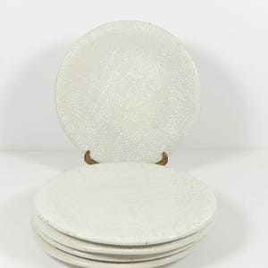 May include: A stack of four white ceramic dinner plates with a textured surface.