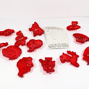 May include: A set of 12 red plastic cookie cutters in various shapes, including a turkey, a reindeer, a snowman, a mushroom, and a cat. The cutters are on a white surface with a white card that says "Cookie Cutter".