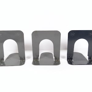 May include: Three metal bookends, two are gray and one is black. Each bookend has a decorative design on the top.