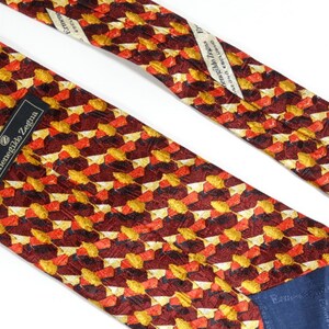 May include: A red, orange, and gold patterned silk tie with a navy blue label that reads "Ermenegildo Zegna".