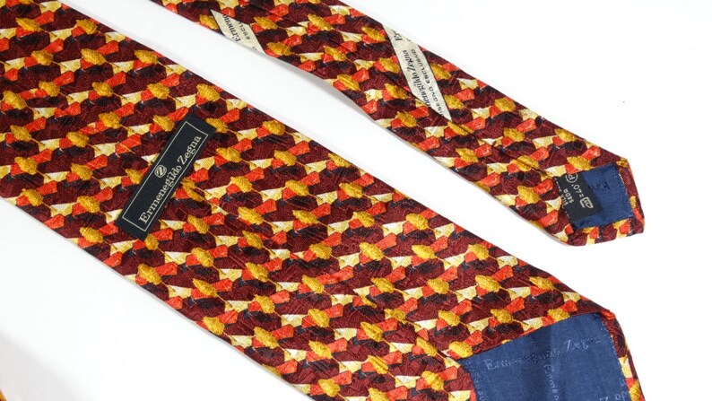 May include: A red, orange, and gold patterned silk tie with a navy blue label that reads "Ermenegildo Zegna".